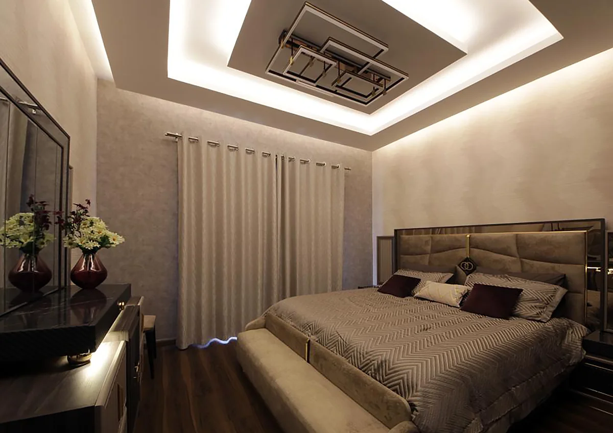 Residential bedroom with warm lighting, decorative ceiling and upholstered headboard